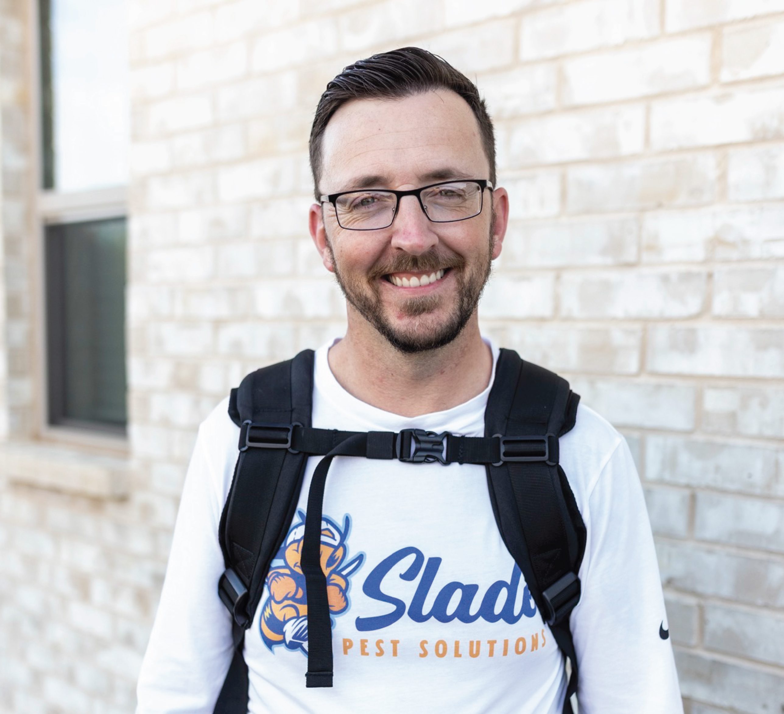 Stephen, owner of Slade Pest Solutions, wearing branded pest control gear and smiling outdoors in front of a residential home.